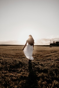 Model walking in a flowing beige linen dress with natural sunlight casting gentle shadows.