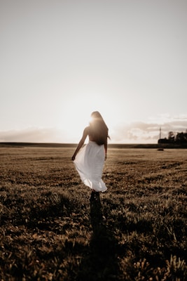 Model walking in a flowing beige linen dress with natural sunlight casting gentle shadows.