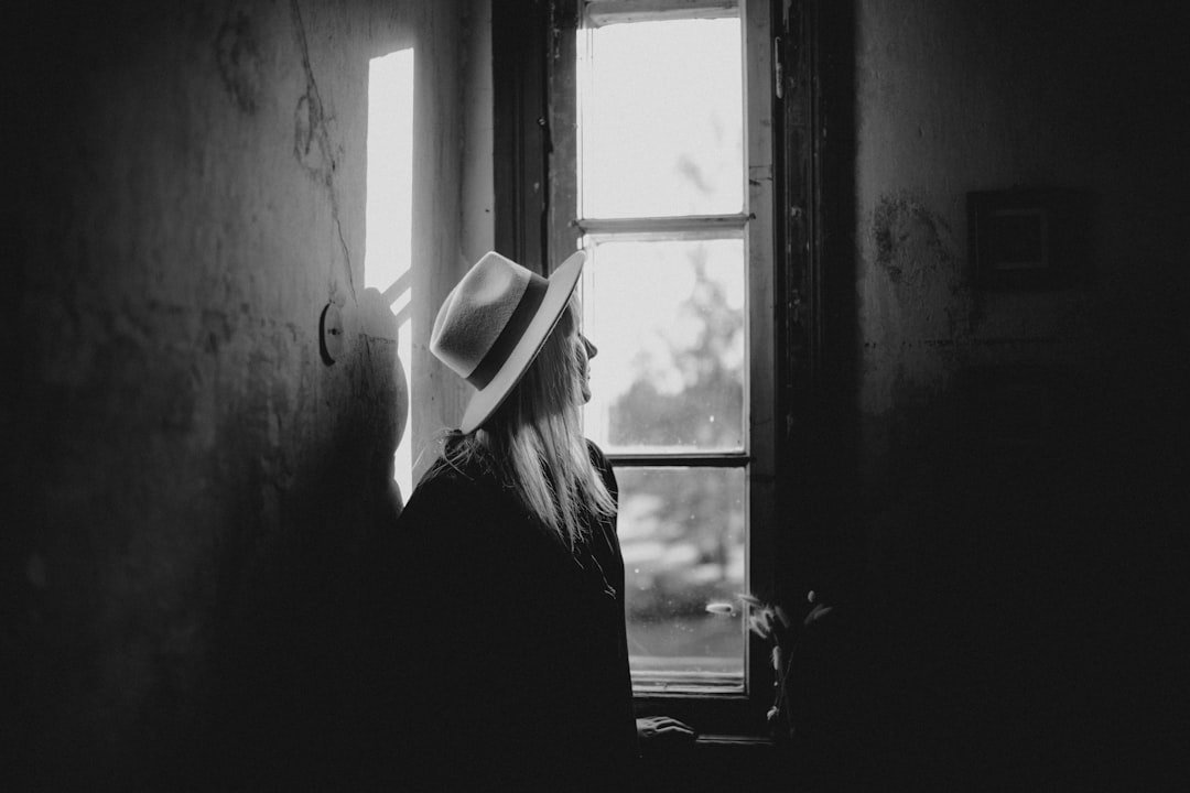 woman in black shirt and white fedora hat standing by the window