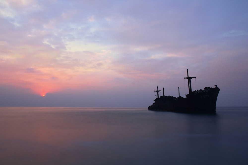 silhouette of person standing on rock formation in the middle of sea during sunset