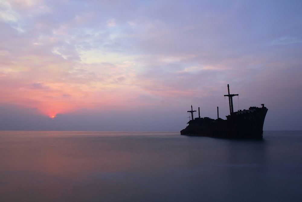 Silhouette einer Person, die während des Sonnenuntergangs auf einer Felsformation mitten im Meer steht