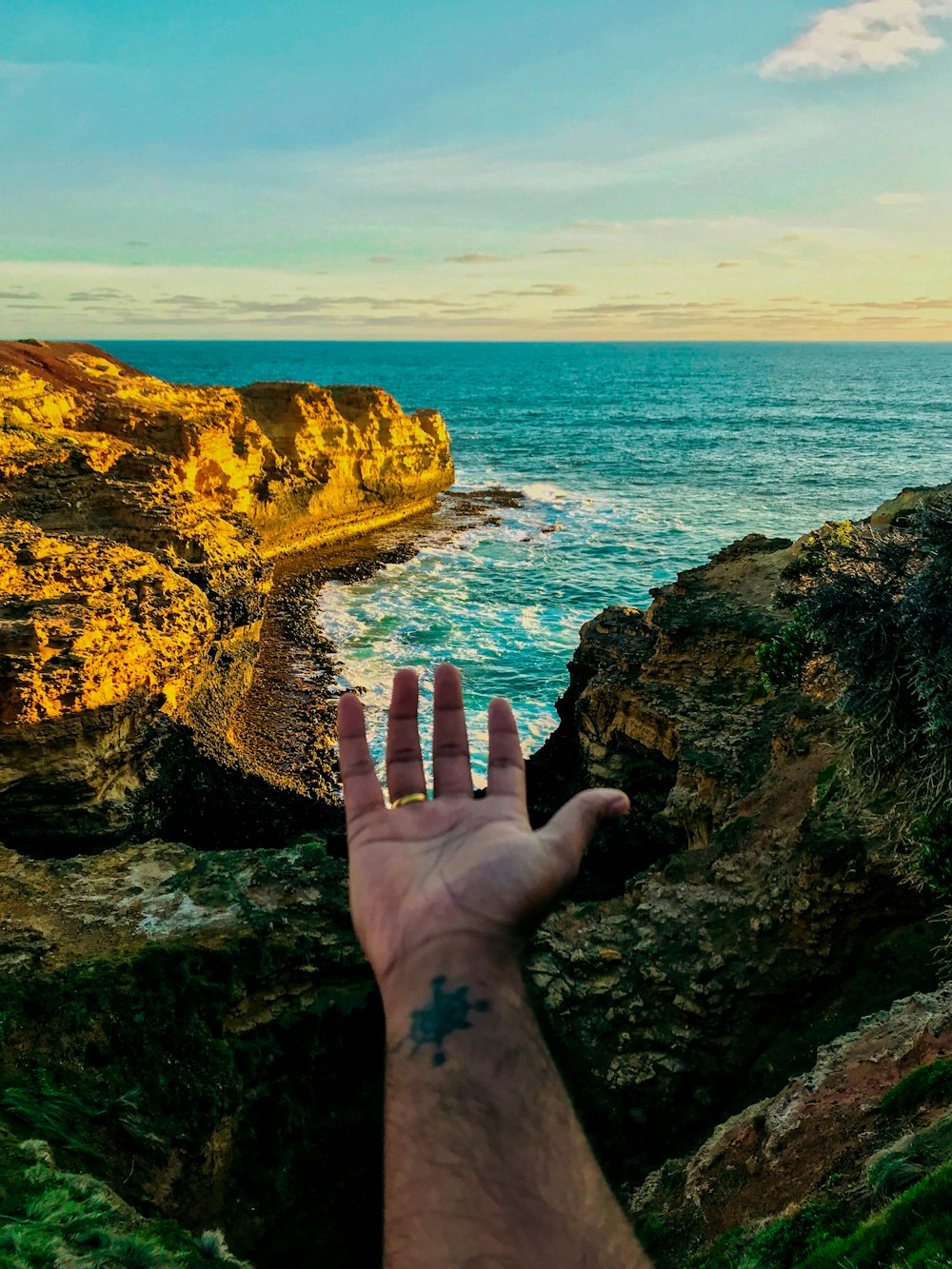 persons hand on brown rock formation near body of water during daytime