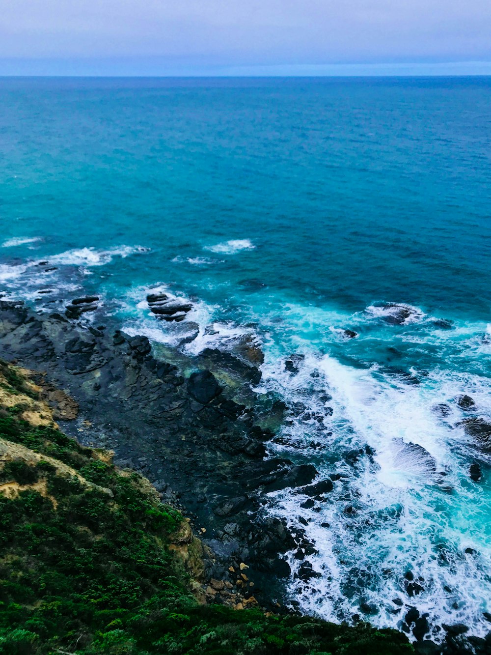 Formazione rocciosa verde e marrone sul mare durante il giorno