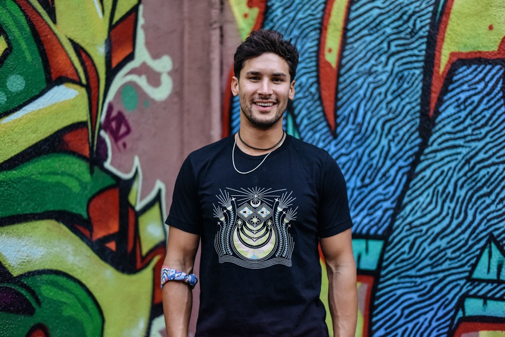 man in black crew neck t-shirt standing beside graffiti wall