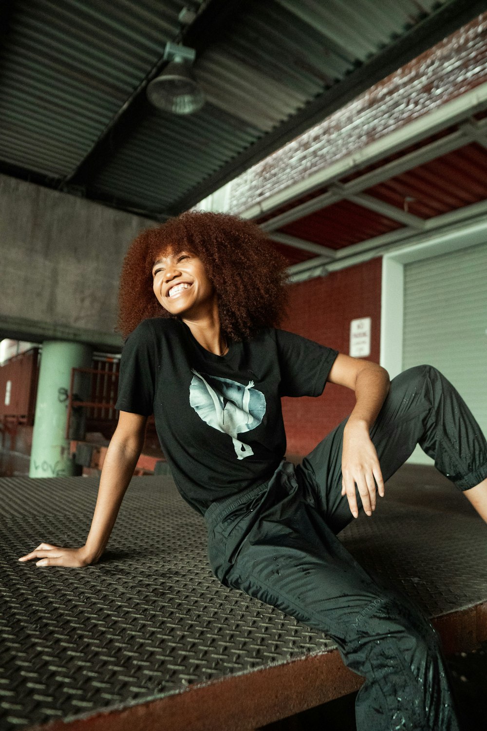 woman in black and white crew neck t-shirt and black pants sitting on black concrete