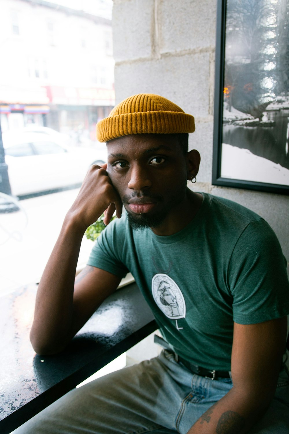 man in green crew neck t-shirt wearing yellow knit cap sitting on chair