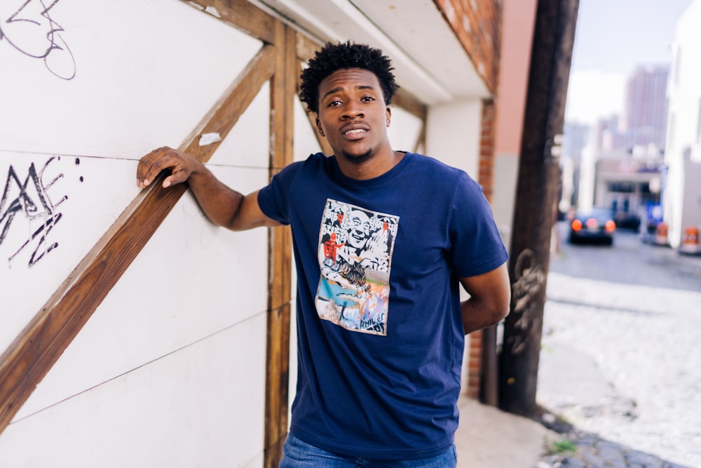 man in blue crew neck t-shirt standing beside white wall during daytime