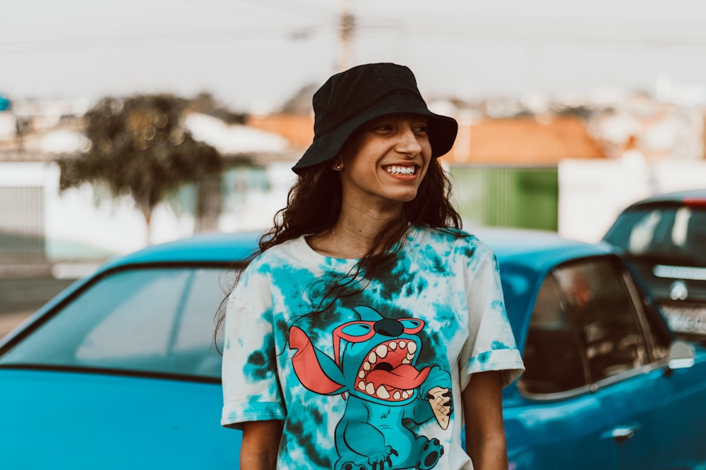woman in white and blue crew neck t-shirt wearing black hat standing beside blue car