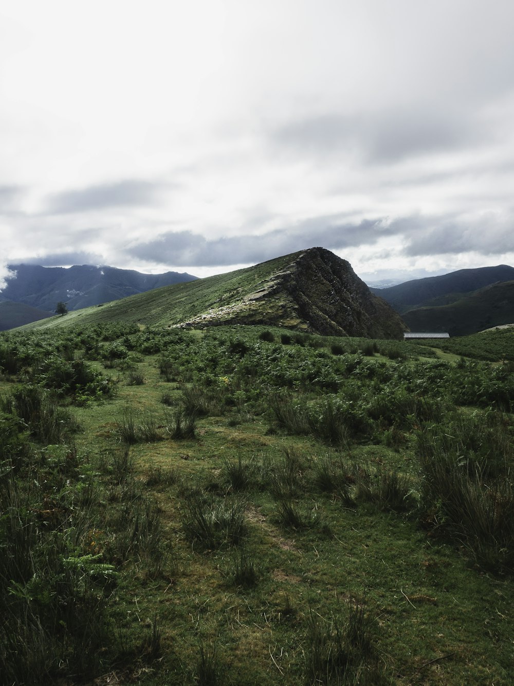 green grass field near mountain under white clouds during daytime