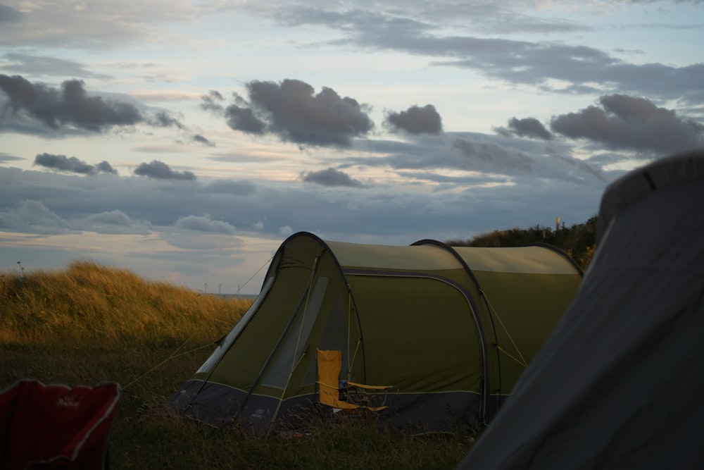 gray tent on green grass field under white clouds during daytime