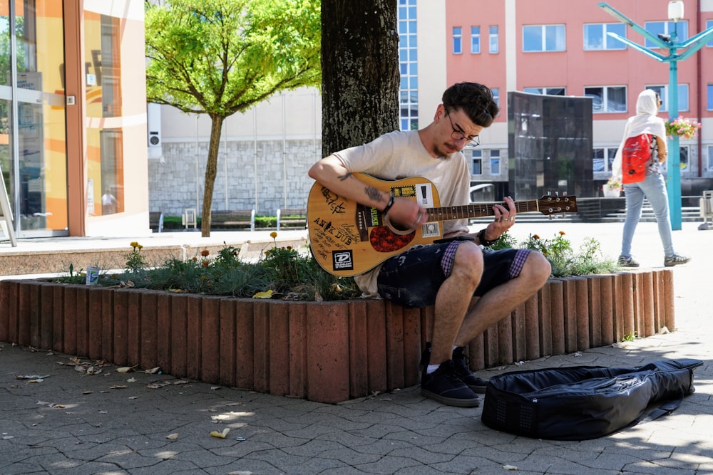 man in white t-shirt playing brown acoustic guitar