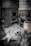 A rusted, old industrial furnace or boiler is situated in a dilapidated, abandoned setting. The ground is covered with debris and dust, including a large, partially visible sack with orange writing and a metallic pipe fitting. The atmosphere suggests neglect and decay.