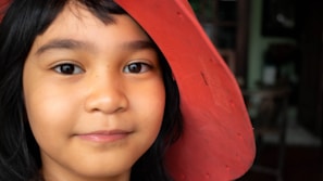 Close-up of a child’s curious eyes peeking out from under a wide-brimmed hat.