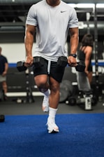 man in gray tank top and black shorts holding black dumbbell