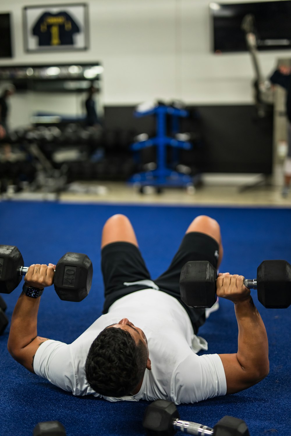 man in white shirt and black shorts holding black dumbbell