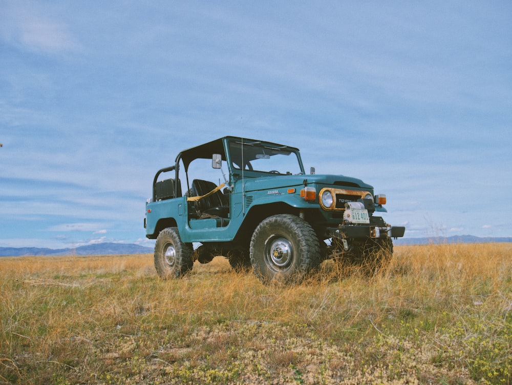 blue and black jeep wrangler on brown field under white clouds during daytime