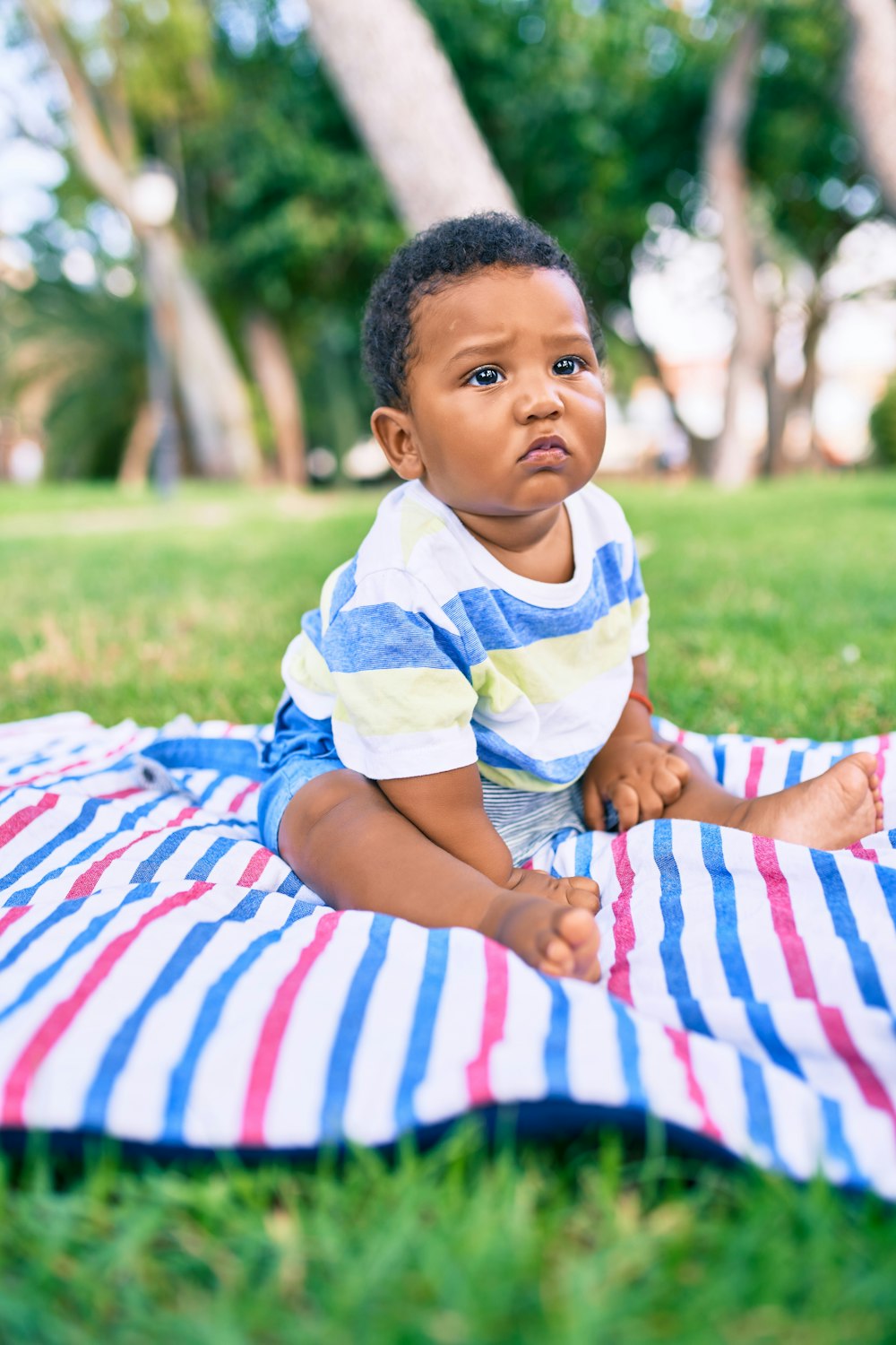 Niño con camisa de rayas blancas y amarillas sentado sobre textil de rayas blancas y rojas durante el día