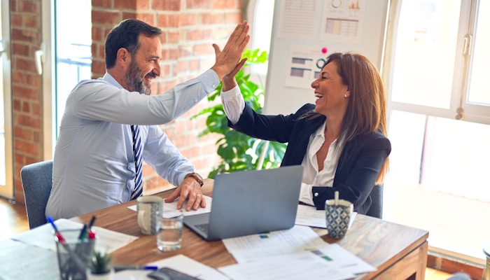 Two middle age business workers smiling happy and confident. Working together with smile on face hand giving high five at the office