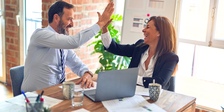 Two middle age business workers smiling happy and confident. Working together with smile on face hand giving high five at the office