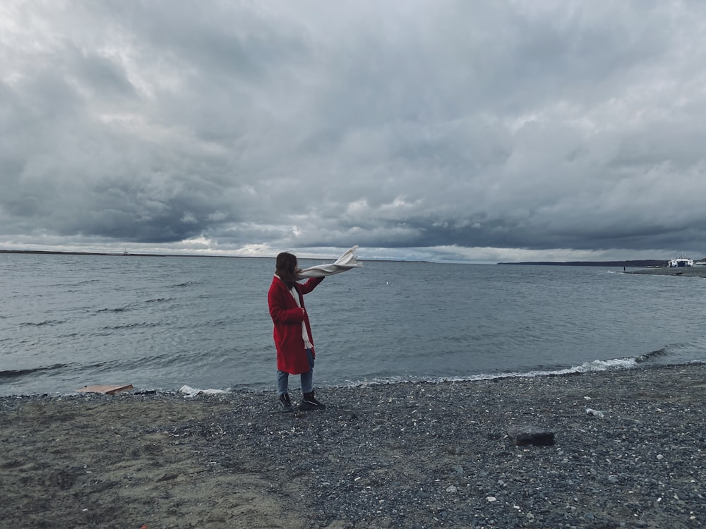 girl in red jacket standing on beach shore during daytime