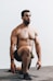topless man in black shorts sitting on brown wooden bench