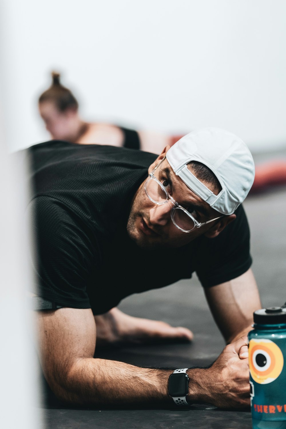 Homme en T-shirt noir à col rond portant une casquette blanche et des lunettes à monture noire