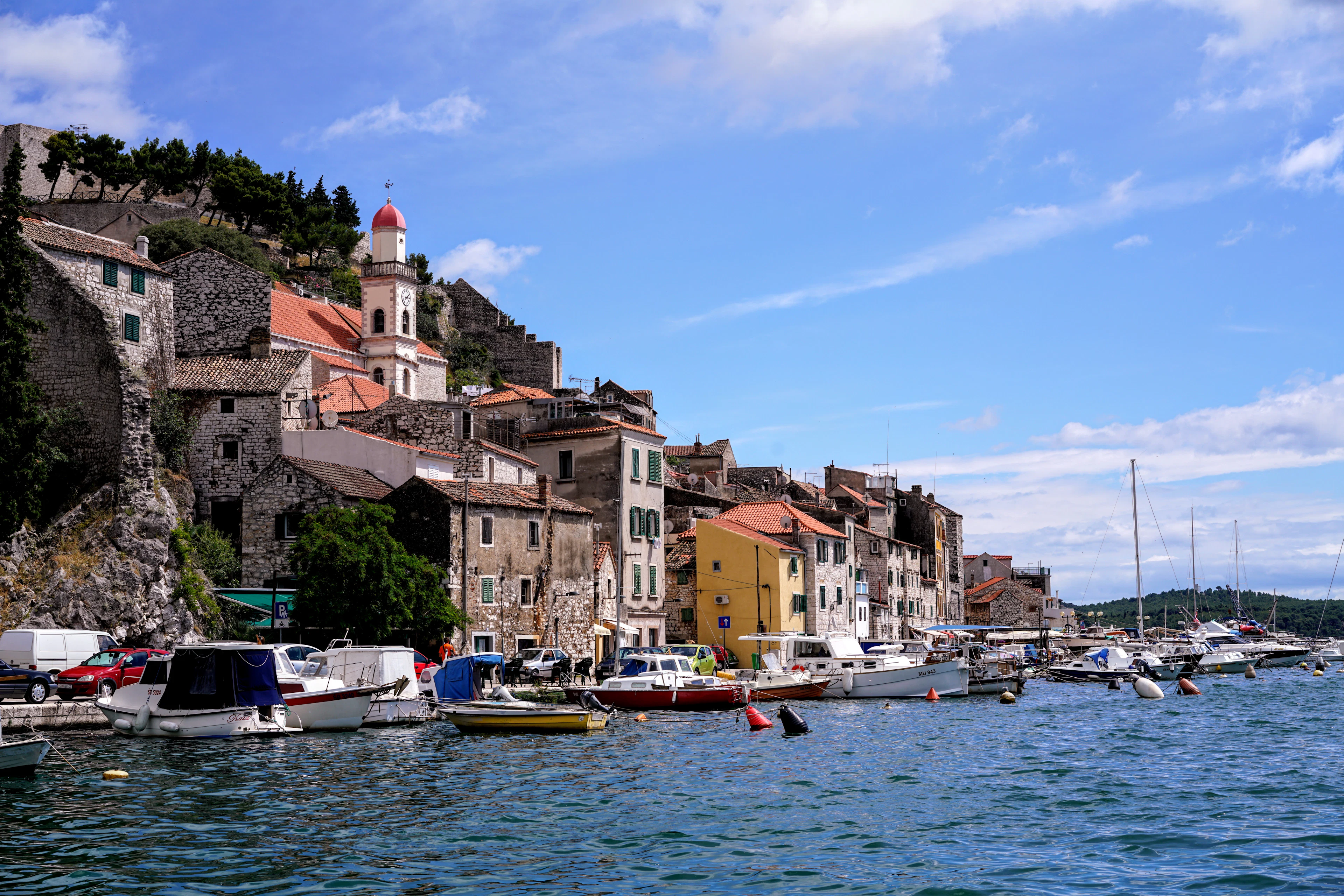 The stone houses and bell tower of Šibenik's old town above a waterfront lined with boats