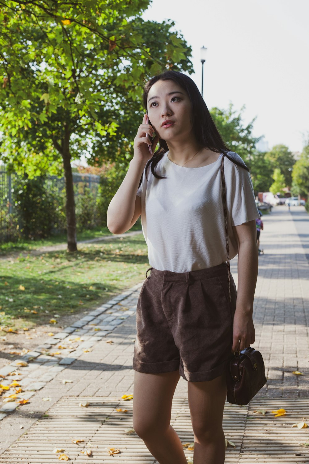 woman in white crew neck t-shirt and brown shorts standing on sidewalk during daytime