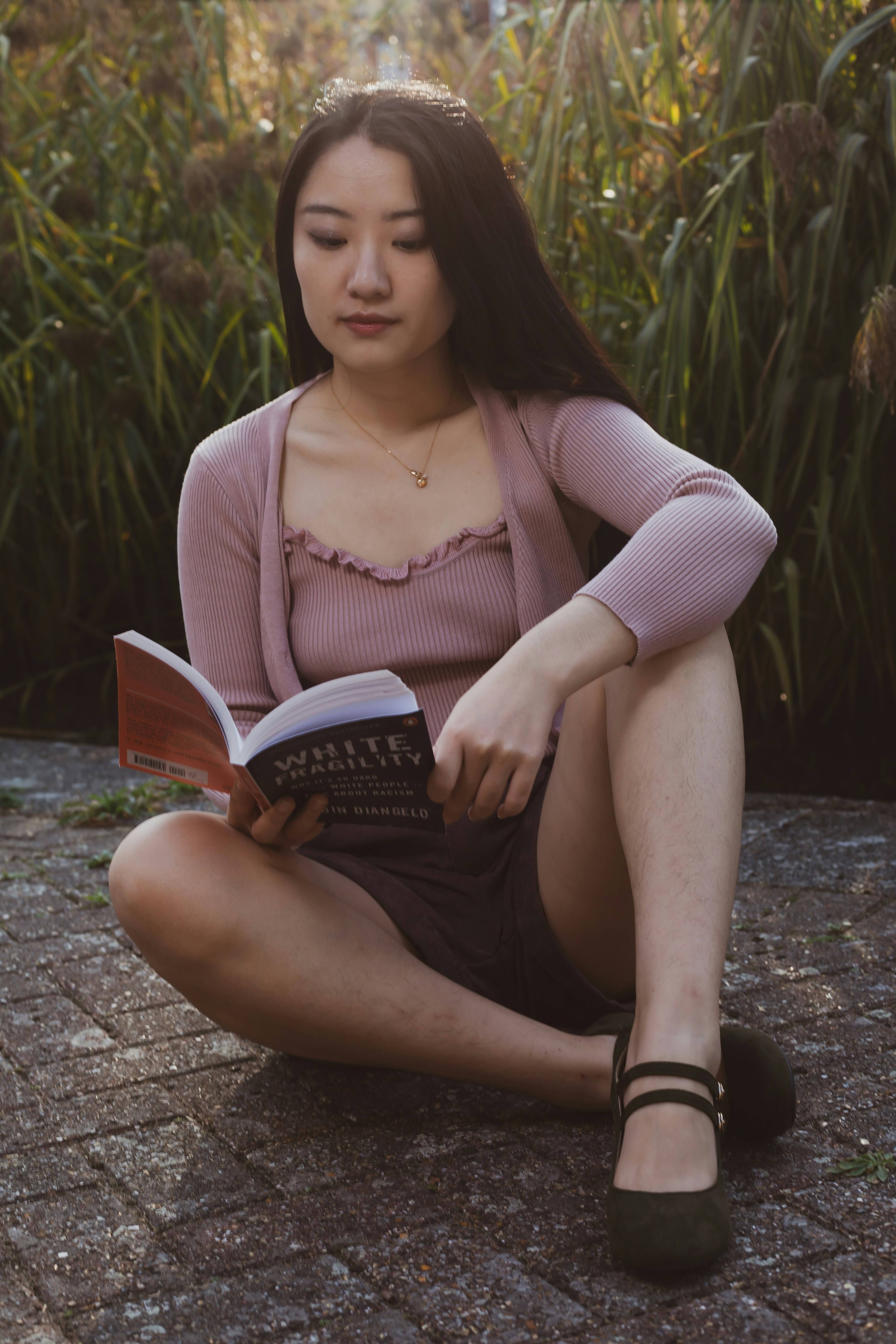 femme en chemise violette à manches longues et jupe noire assise sur un sol en béton