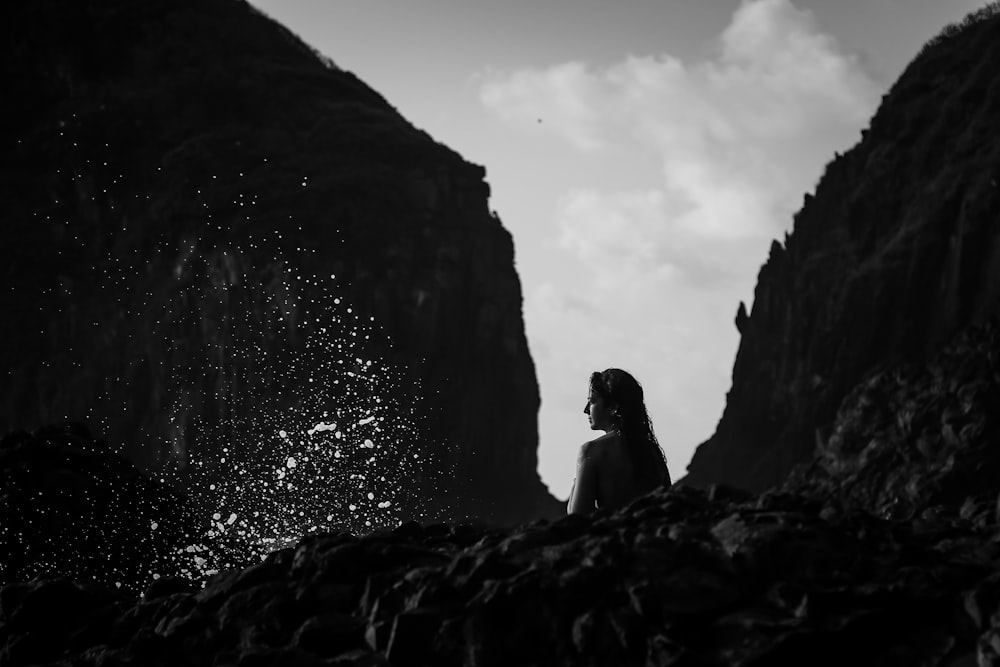 grayscale photo of woman sitting on rock formation