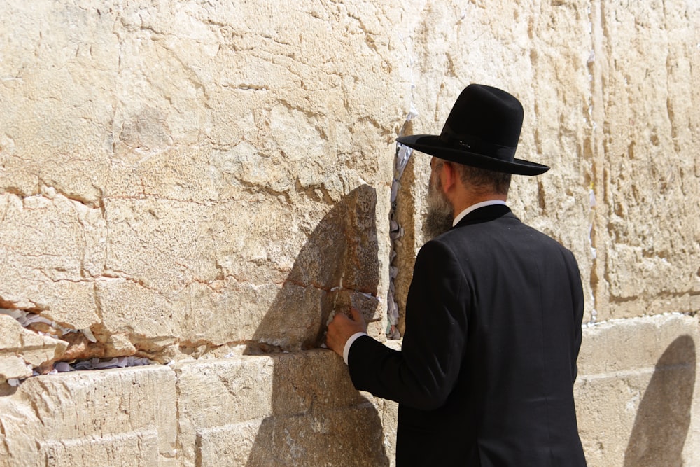 man in black long sleeve shirt and brown cowboy hat standing beside brown concrete wall during