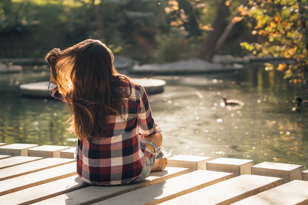 woman in red white and black plaid shirt sitting on wooden dock during daytime