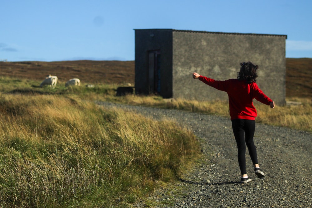 woman in red long sleeve shirt and black pants walking on gray concrete pathway during daytime