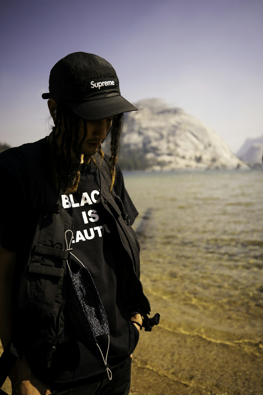 茶色の砂の上に立つ黒い帽子をかぶった黒と白のクルーネックTシャツの男性