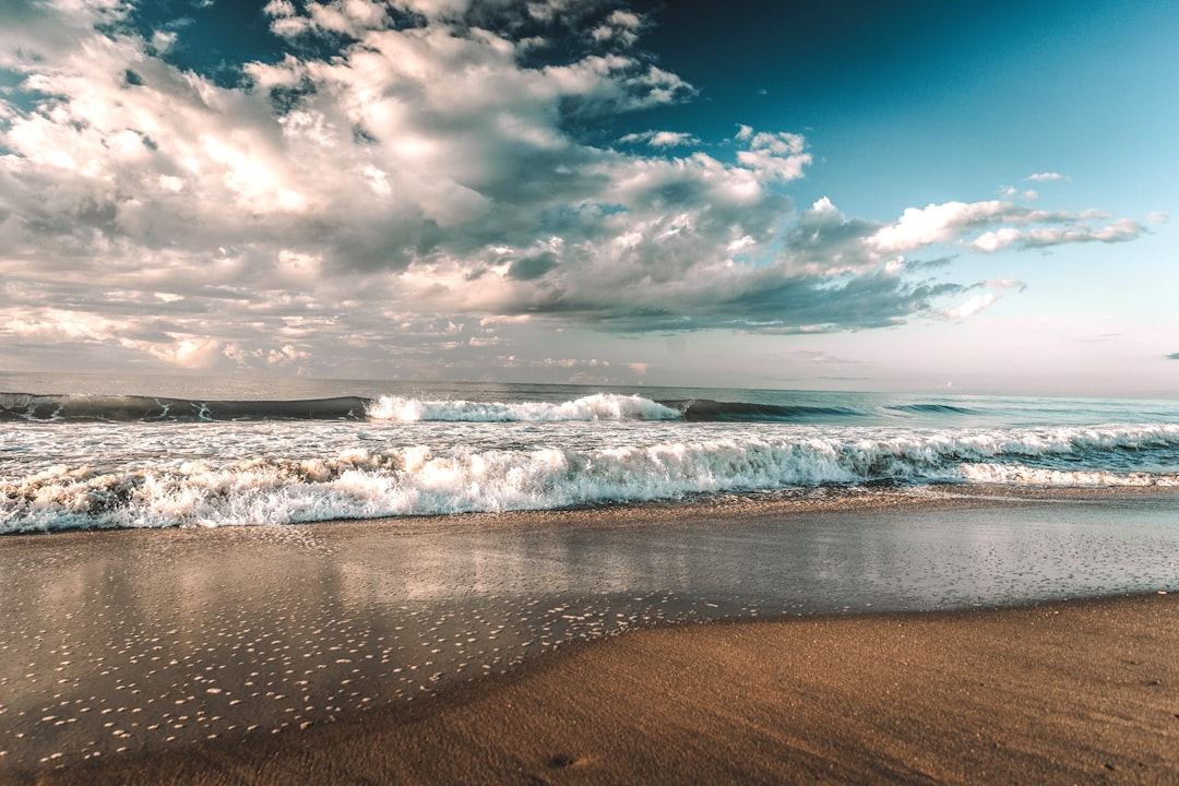 sea waves crashing on shore under blue and white cloudy sky during daytime