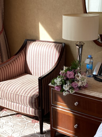 A cozy corner with a soft beige armchair, a stack of books, and a delicate vase of fresh flowers on a wooden side table.
