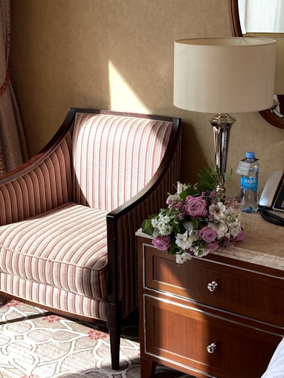 A sunlit corner of a living room featuring a velvet armchair, soft throw pillows, and a marble side table topped with fresh flowers.