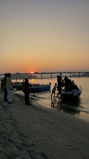 Sunset over a serene riverbank in Andhra Pradesh, with fishermen preparing their boats.