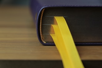 A close-up of a vibrant purple and gold book spine resting on a textured wooden table, evoking a sense of craftsmanship and permanence.
