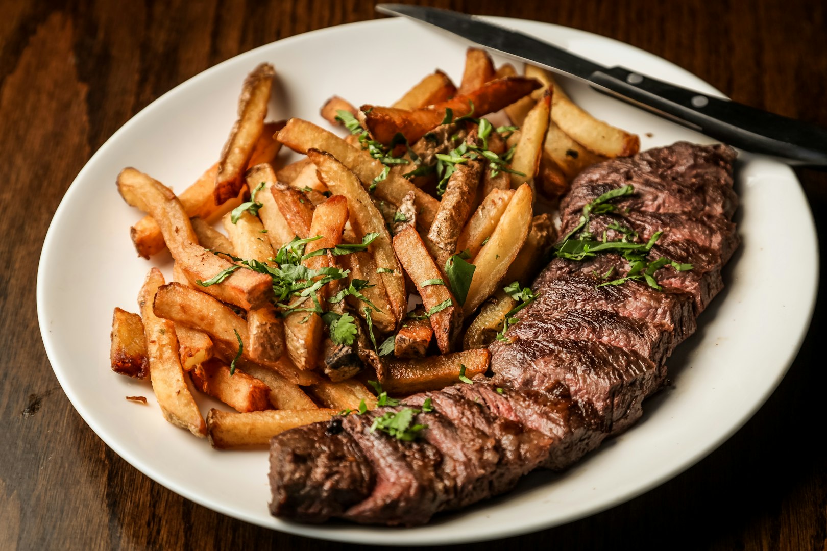 Beautifully marbled ribeye steak with fresh rosemary and cracked pepper on a dark wooden surface