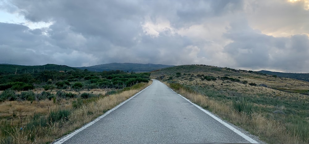 gray asphalt road between green grass field under white cloudy sky during daytime