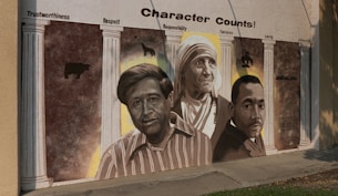 A mural features three prominent figures, each highlighted within columns that emphasize various character traits like trustworthiness, respect, responsibility, fairness, caring, and citizenship. The artwork reflects values of integrity and moral strength.