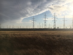 electric towers on brown grass field under blue sky during daytime