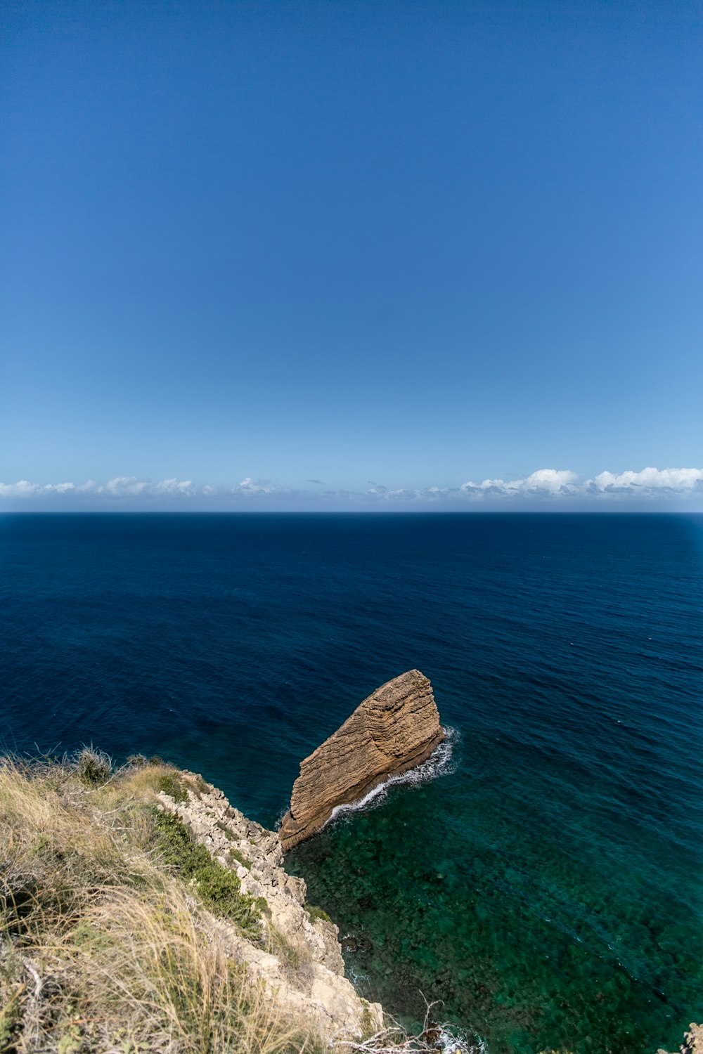 brown rock formation on sea under blue sky during daytime