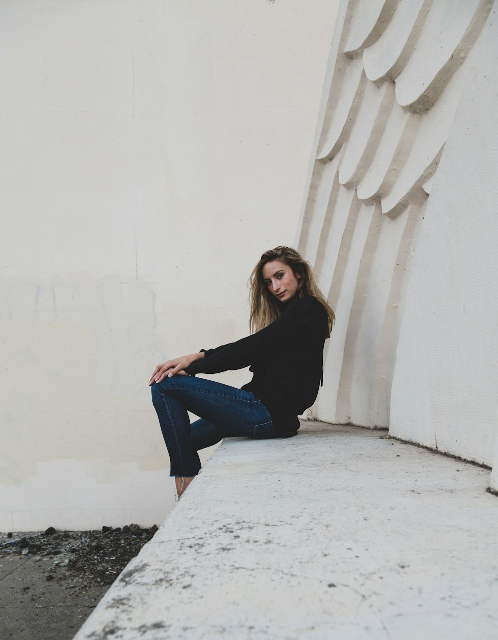 woman in black long sleeve shirt and blue denim jeans sitting on white concrete bench