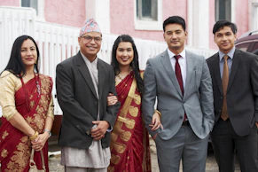 man in black suit standing beside woman in red and gold sari