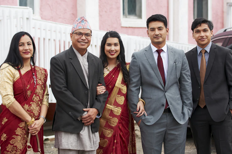 man in black suit standing beside woman in red and gold sari