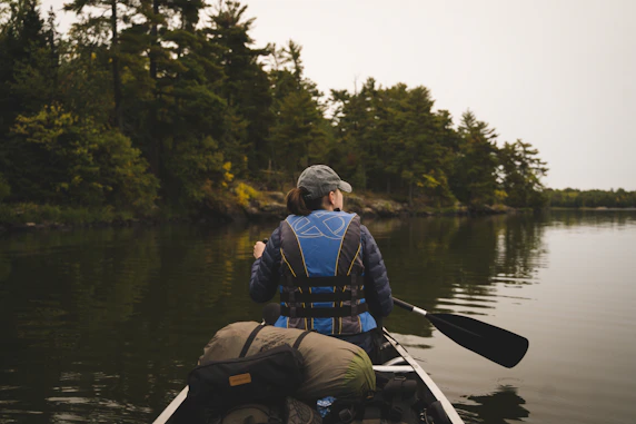 Minnesota woman in blue jacket and black backpack riding on aluminum canoe on Minnesota lake daytime