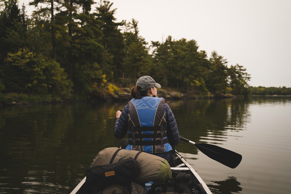 man in blue jacket and black backpack riding on white kayak on river during daytime