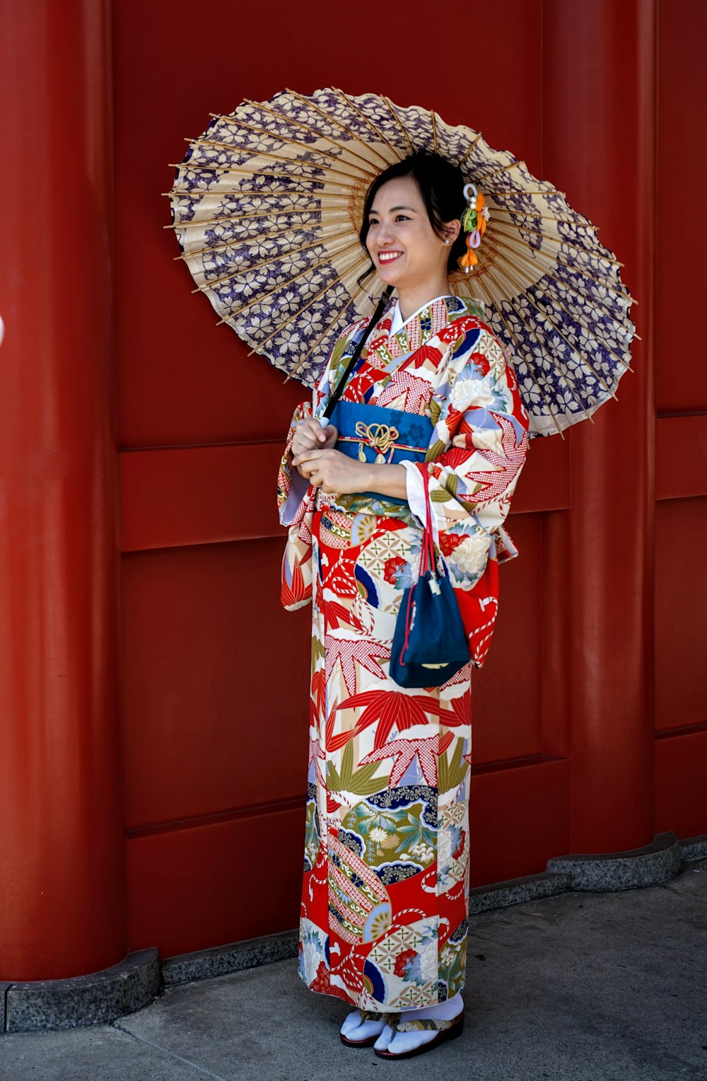 Femme en kimono rouge, blanc et bleu debout près du mur rouge